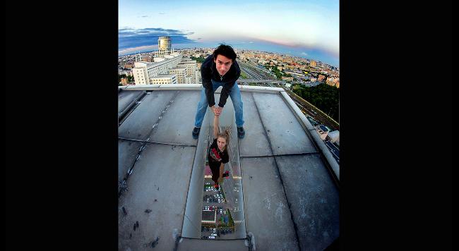 Иван Семенов держит свою девушку над Москвой, стоя на крыше бизнес-центра, Россия.