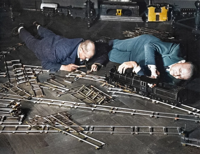 Два пожилых мужчины на полу в здании Общества игрушечных железных дорог. Один регулирует розетку небольшим молоточком, второй ремонтирует двигатель паровоза. Берлин, Германия, 1931 год.