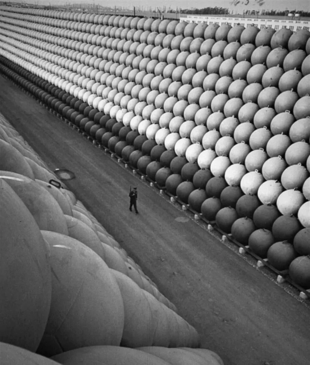 8. Охранник идёт по шоссе US Highway 101, где стоят высокие стопки полых железных поплавков, на которых во время последней войны были подвешены противолодочные сети для защиты портов США, 1953 год 8. Охранник идёт по шоссе US Highway 101, где стоят высокие стопки полых железных поплавков, на которых во время последней войны были подвешены противолодочные сети для защиты портов США, 1953 год